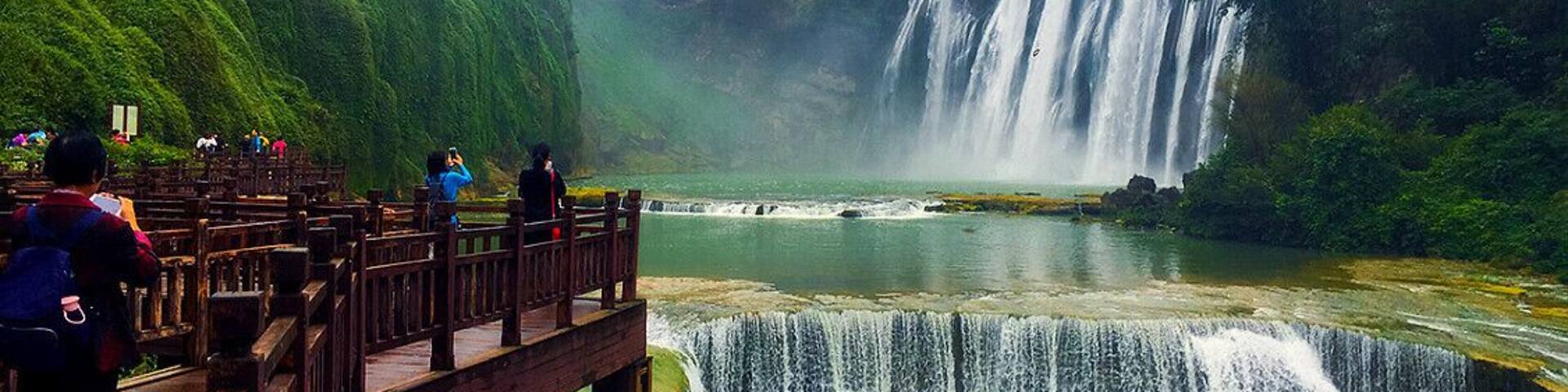 Una cascada se precipita sobre un risco rocoso hacia un río, rodeada de abundante vegetación.