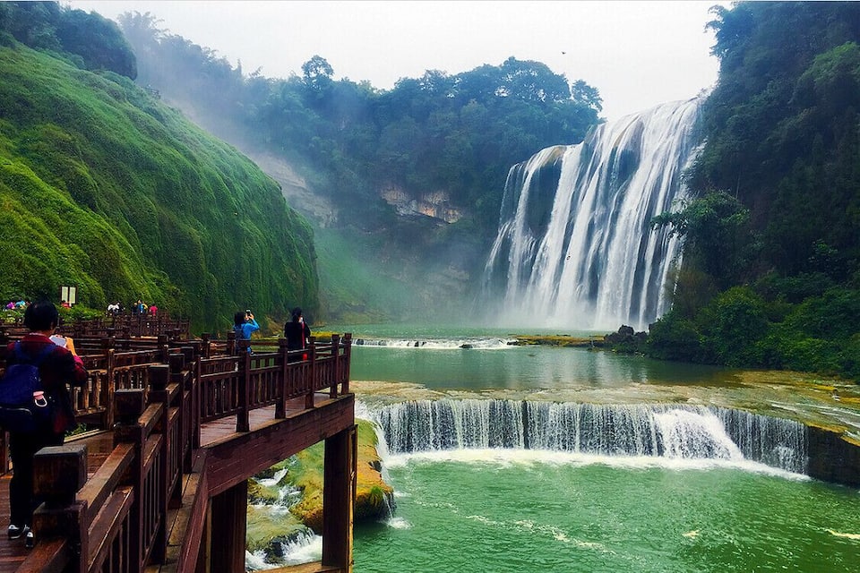Una cascata che si getta da una rupe rocciosa in un fiume, circondata da vegetazione lussureggiante.