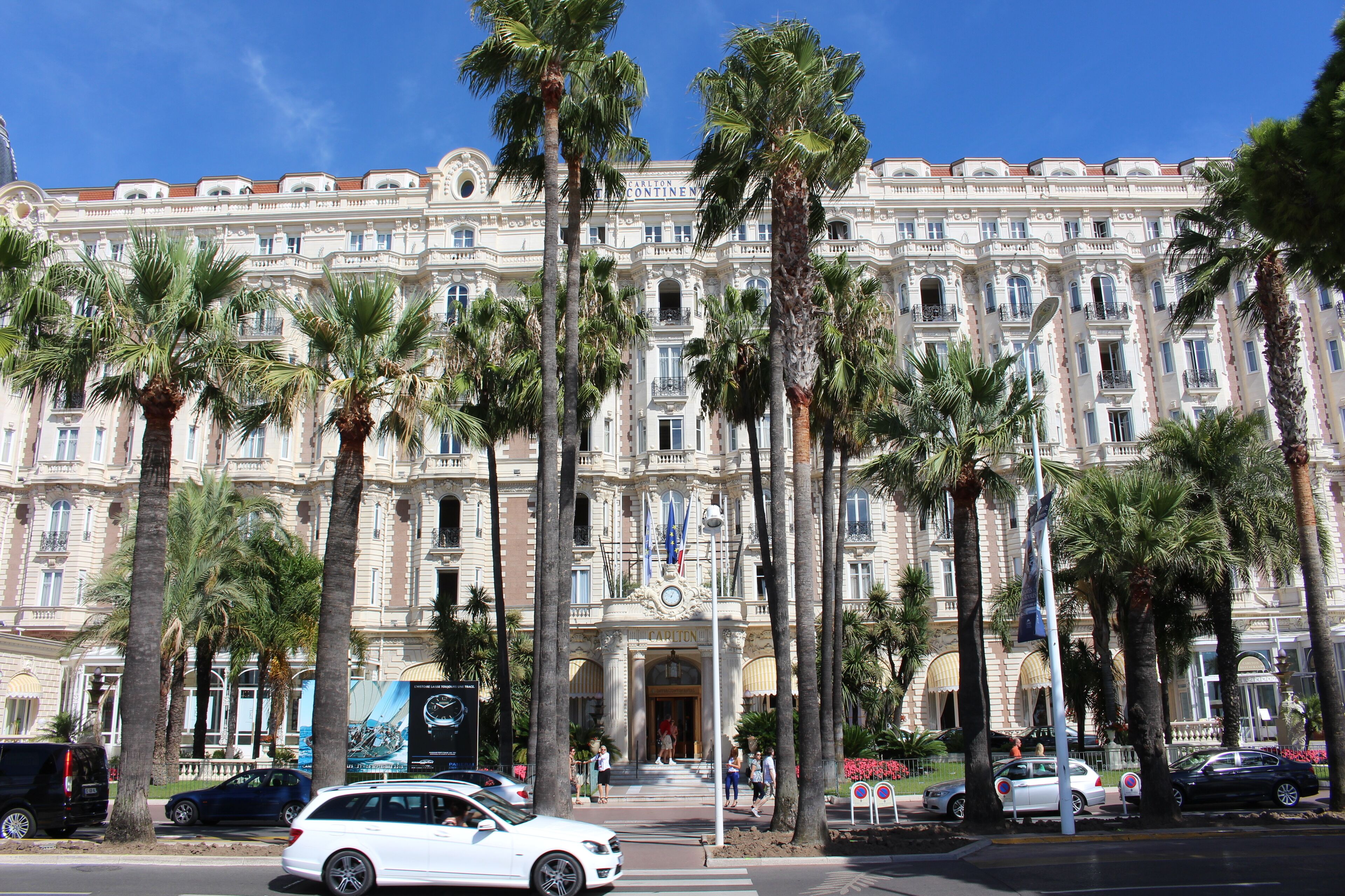 A grand building with a classical facade, palm trees, and a clear blue sky.