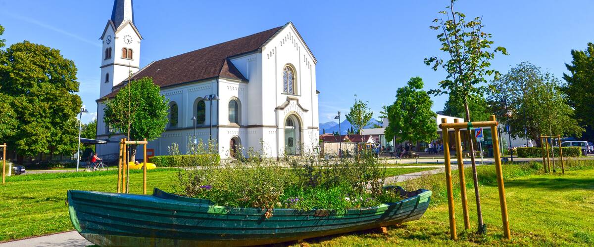 A church with a tall steeple, a green boat in a grassy area, and a clear blue sky.