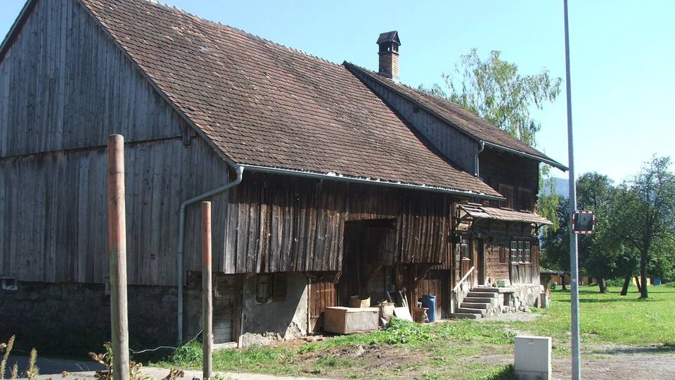 An old wooden barn with a weathered exterior, a chimney, and a porch with steps leading up to it.