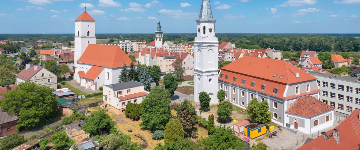 A town with prominent red-roofed buildings, a church with a tall bell tower, and a large white church with a spire.