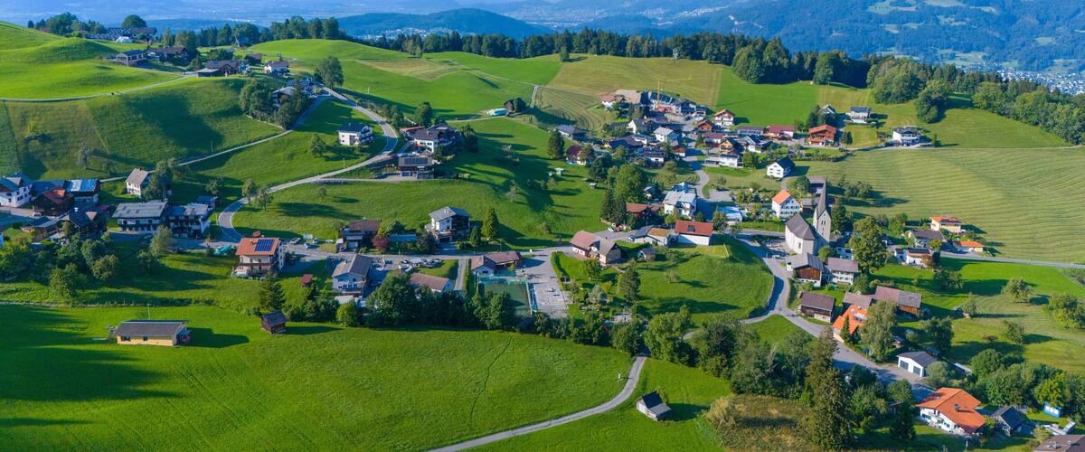 A rural village with houses and roads surrounded by green hills and mountains.