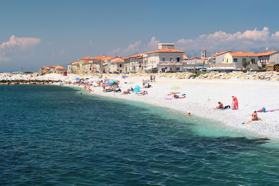Uma vila costeira com uma praia de areia branca, águas turquesa cristalinas e edifícios históricos com telhados de terracota.