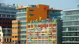 Un bâtiment moderne dont la façade est ornée de sculptures colorées représentant des personnes en train d’escalader ou de danser.