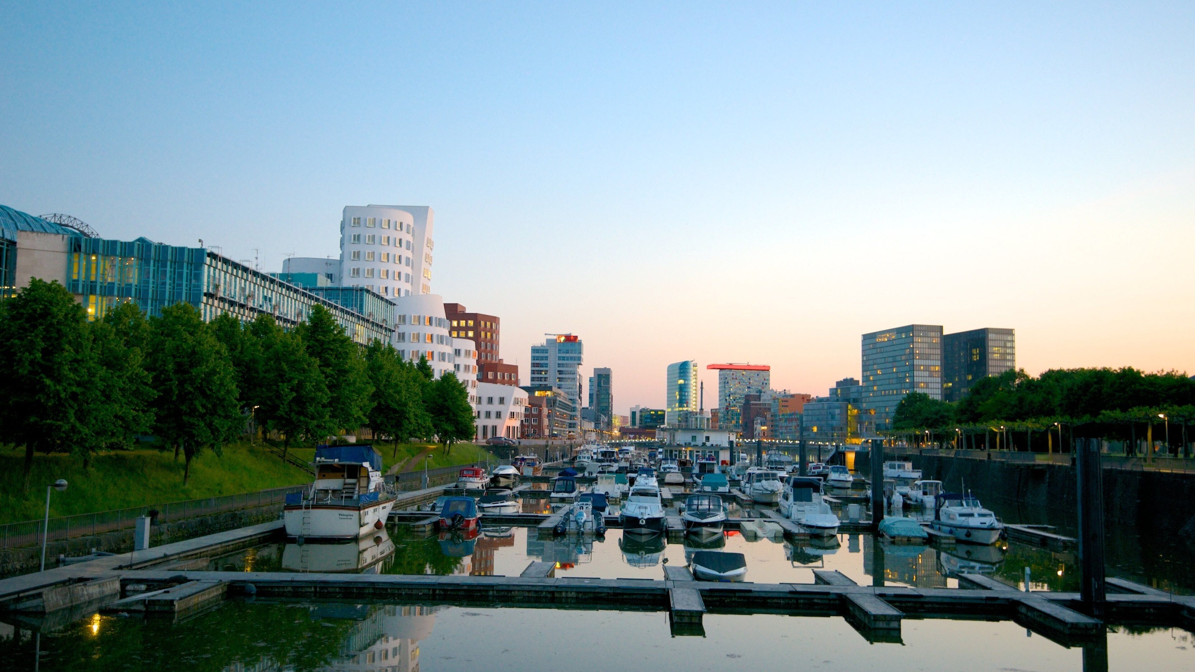 A marina with boats docked, surrounded by modern buildings and trees.
