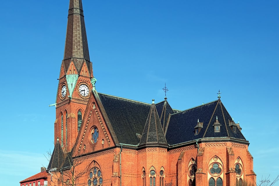 A large red brick church with a tall steeple and a clock tower.