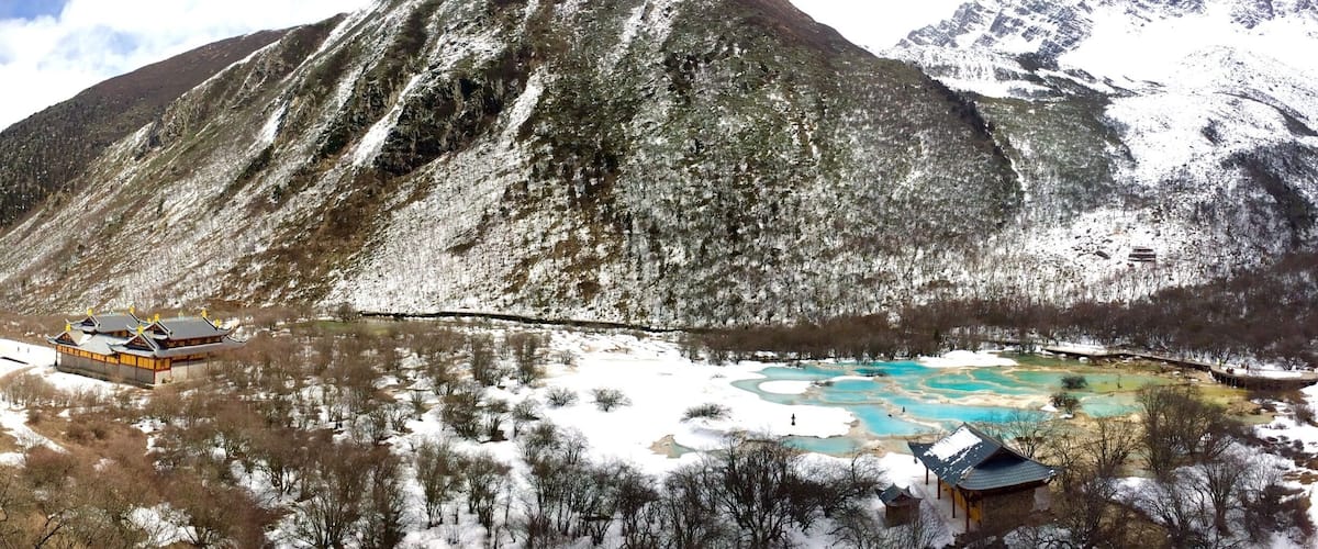 A snow-covered mountain with a traditional building and a hot spring area.