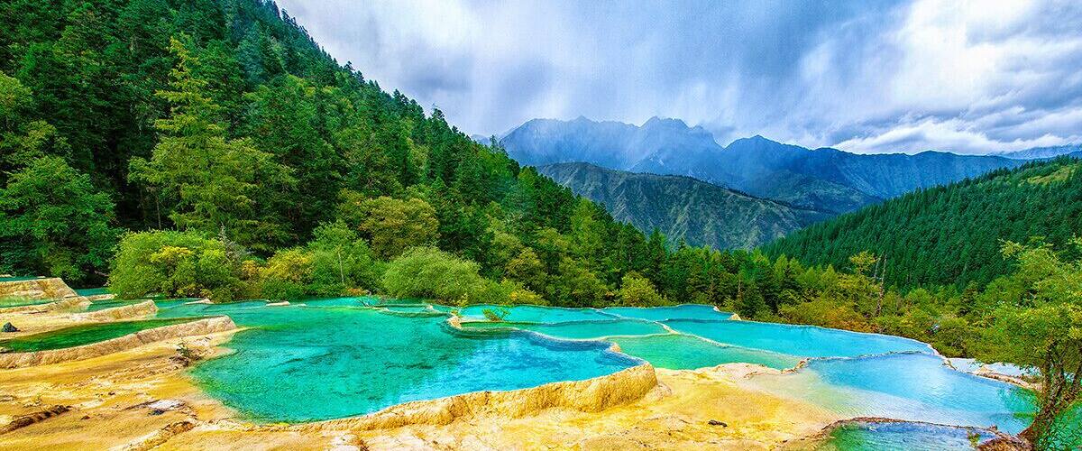 Piscinas escalonadas de agua turquesa rodeadas de exuberante bosque y montañas.