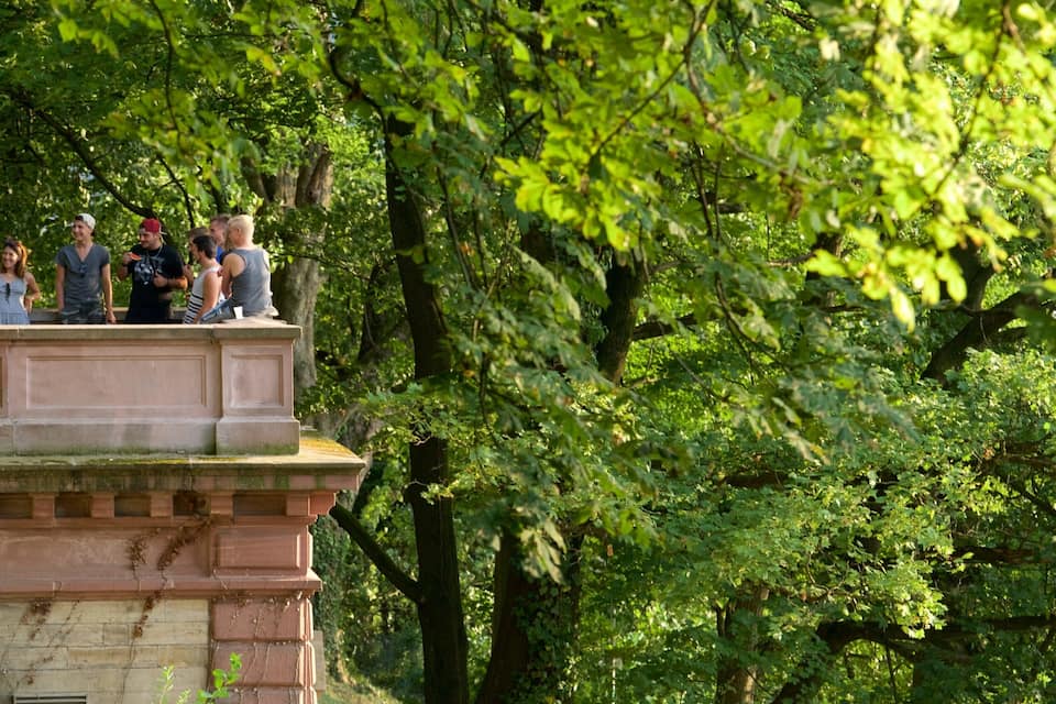 A stone balustrade with people standing on it, surrounded by lush green trees.