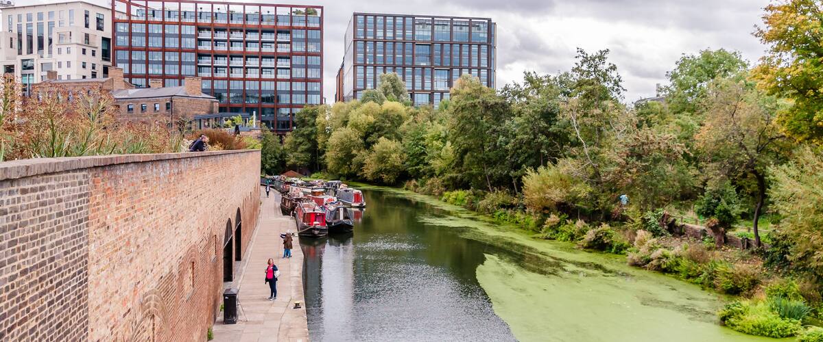 A river with boats, a brick wall, and modern buildings in the background.
