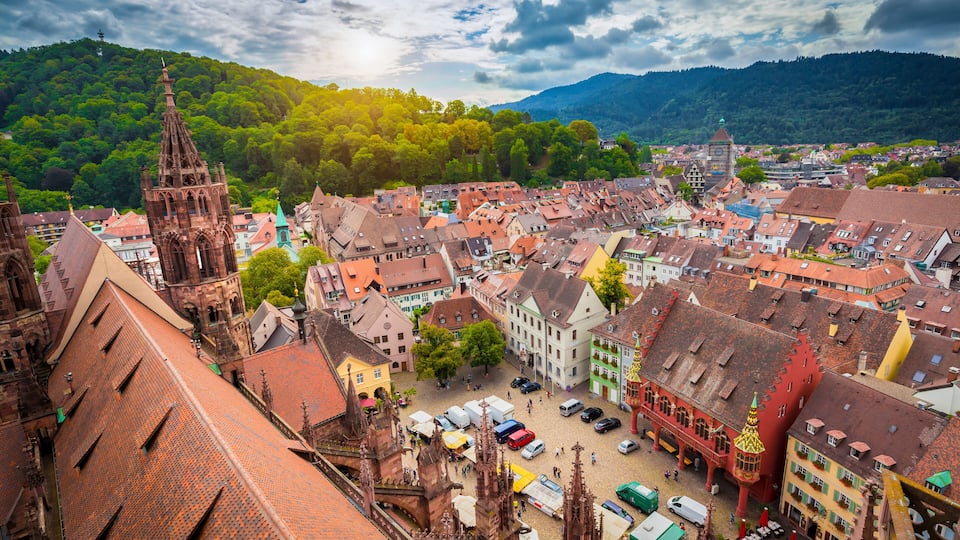 A historic town with a prominent church tower, colorful buildings, and a mountainous backdrop.