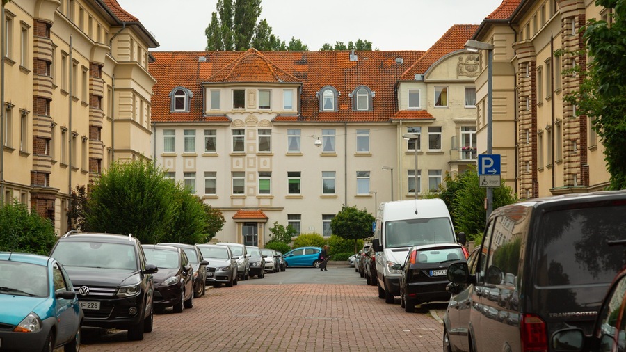 Eine Reihe geparkter Autos an einer straßebewehrten Straße, im Hintergrund ein großes Gebäude.