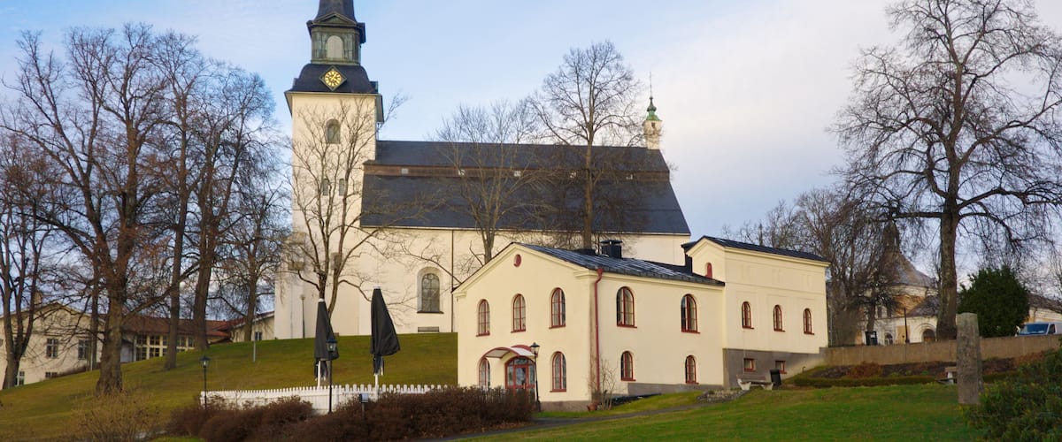 A church with a tall steeple and a clock, surrounded by trees and a grassy area.