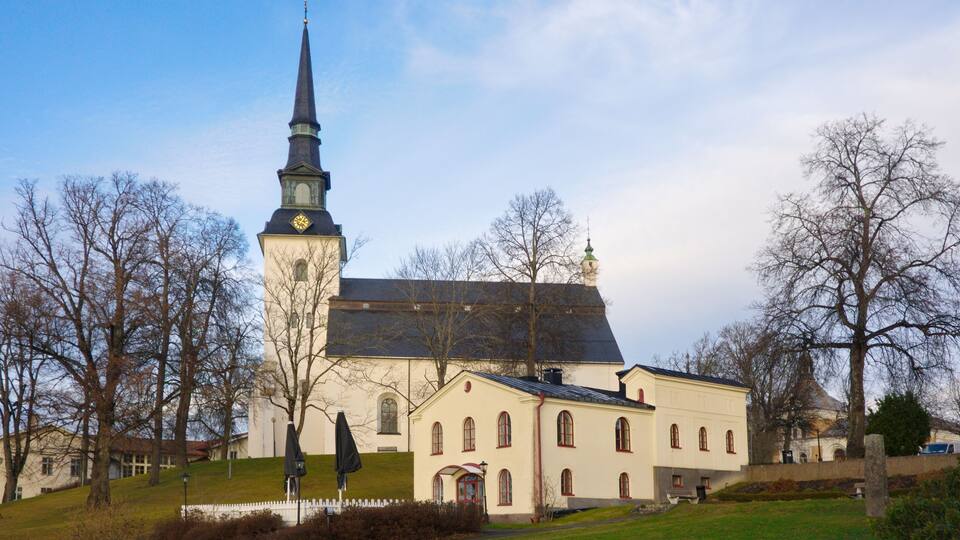 A church with a tall steeple and a clock, surrounded by trees and a grassy area.