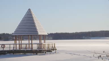 Um gazebo coberto de neve em um lago congelado, com céu claro.