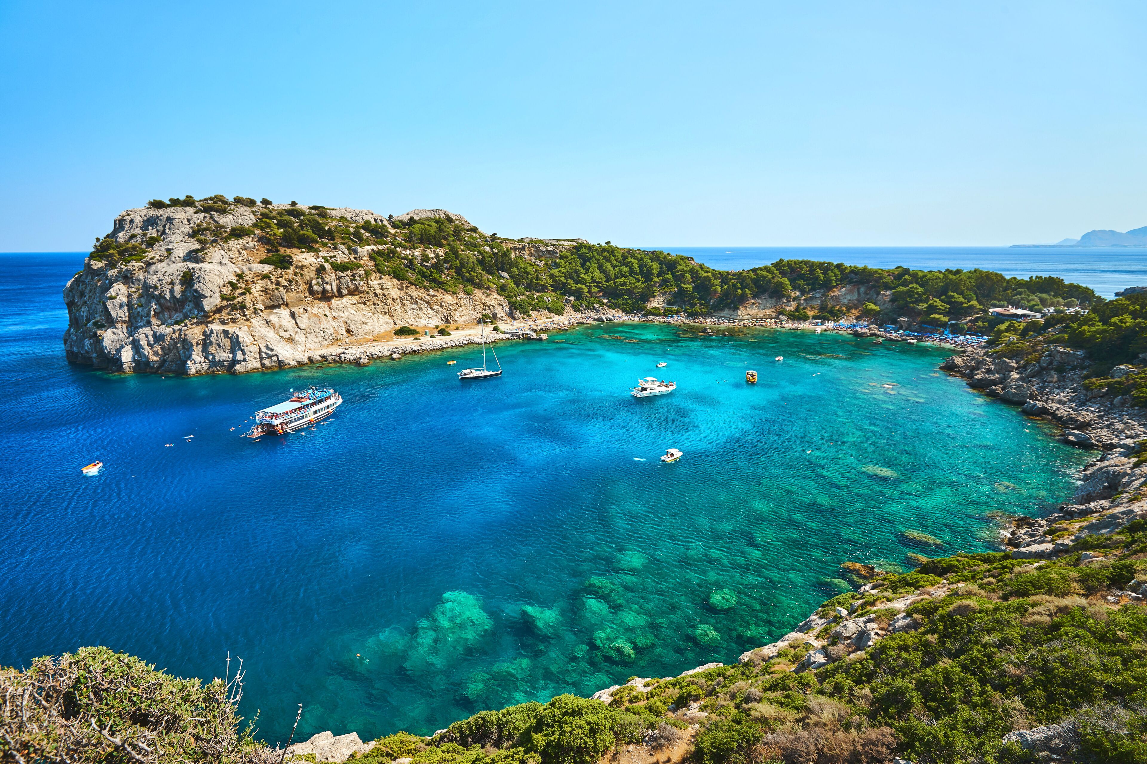 A coastal bay with clear turquoise waters, rocky cliffs, and a small island with vegetation.