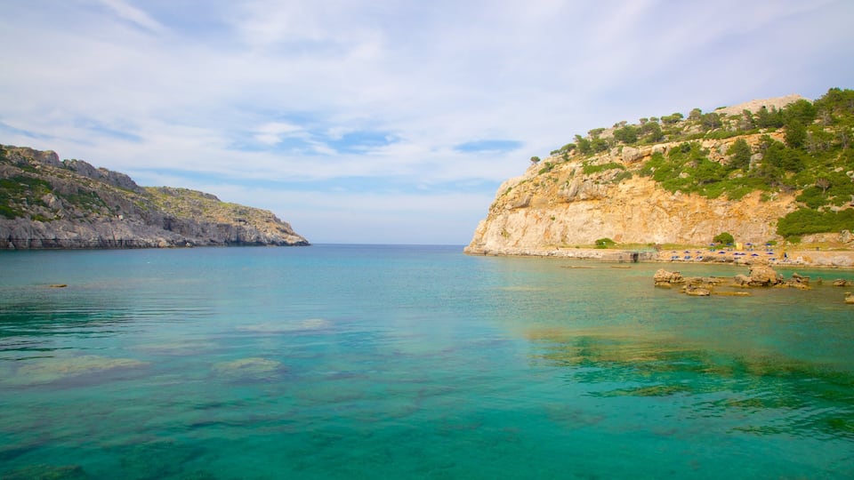 A coastal landscape with clear turquoise waters, rocky cliffs, and sparse vegetation.