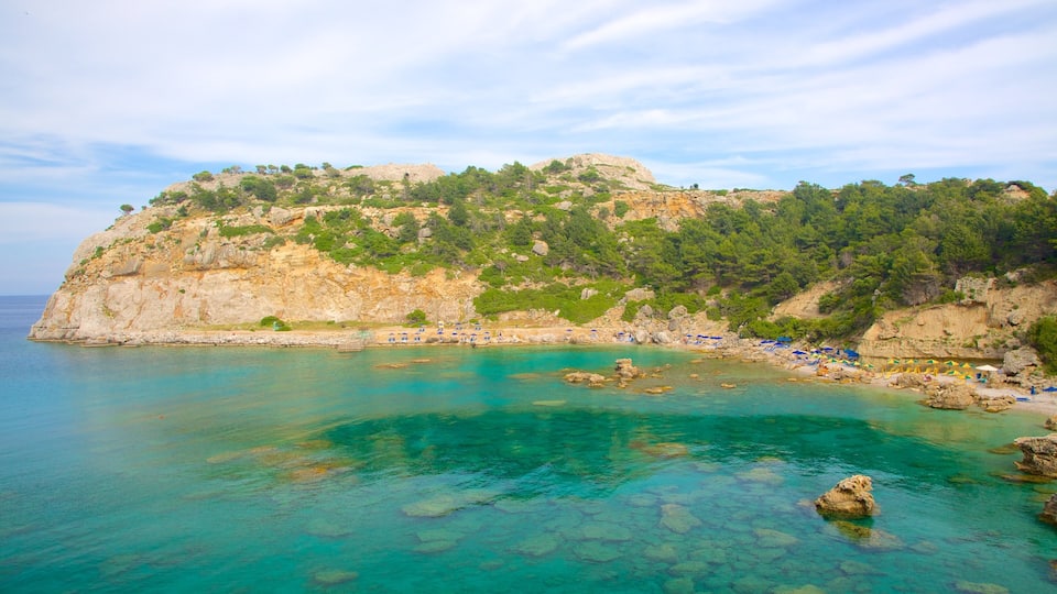A coastal landscape with clear turquoise waters, rocky cliffs, and a beach with umbrellas.