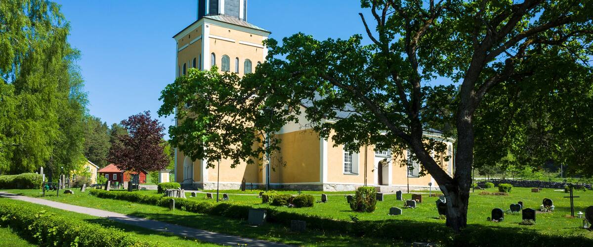A church with a tall tower and a large tree in front.