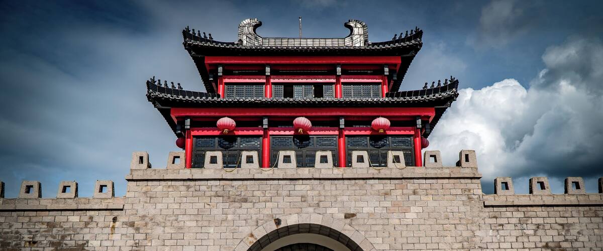 A traditional Chinese gate with a red and black roof, brick walls, and an arched entrance.