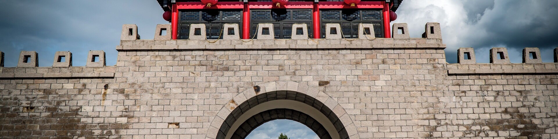 A traditional Chinese gate with a red and black roof, brick walls, and an arched entrance.