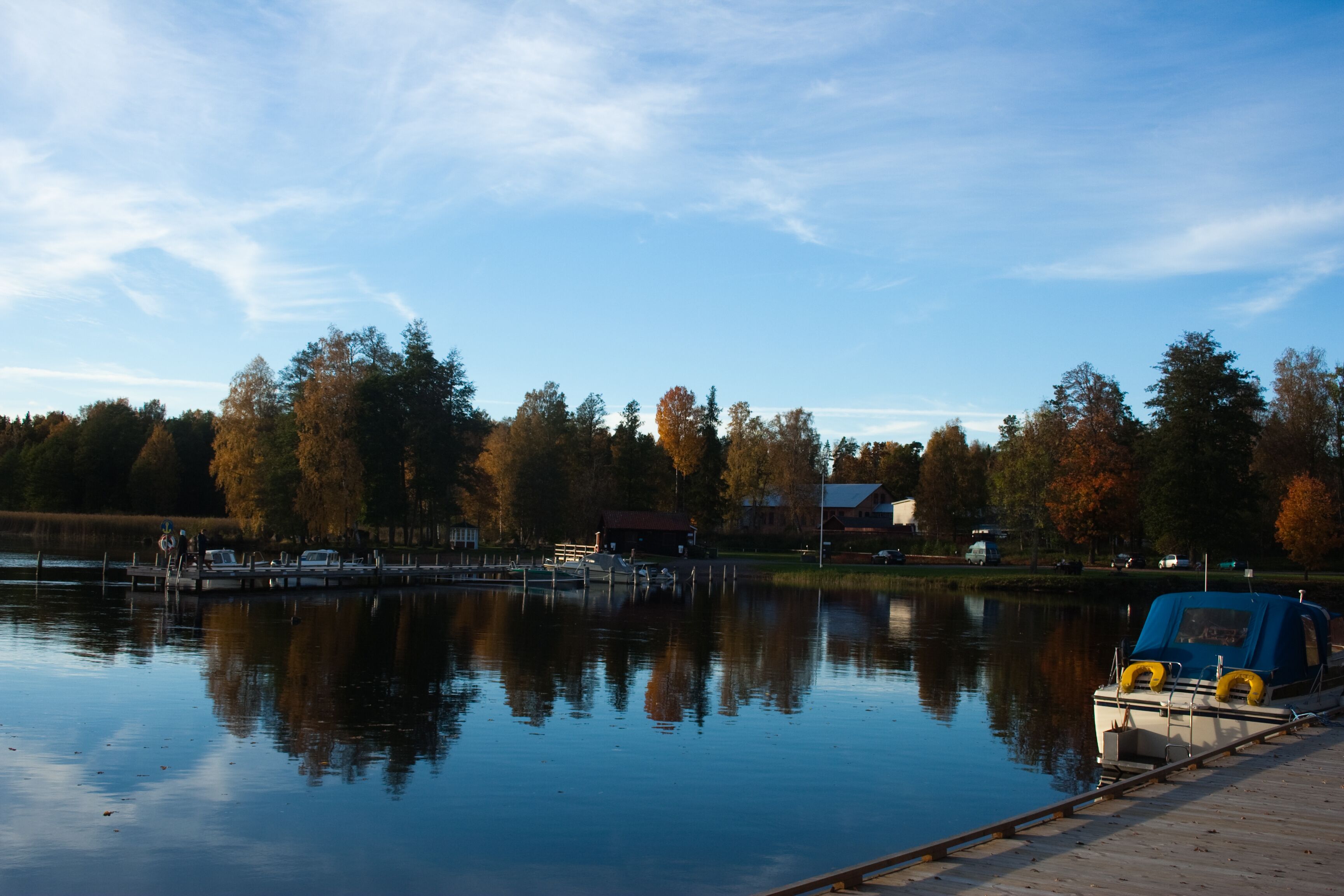 A calm lake with a dock, boats, and autumn trees in the background.