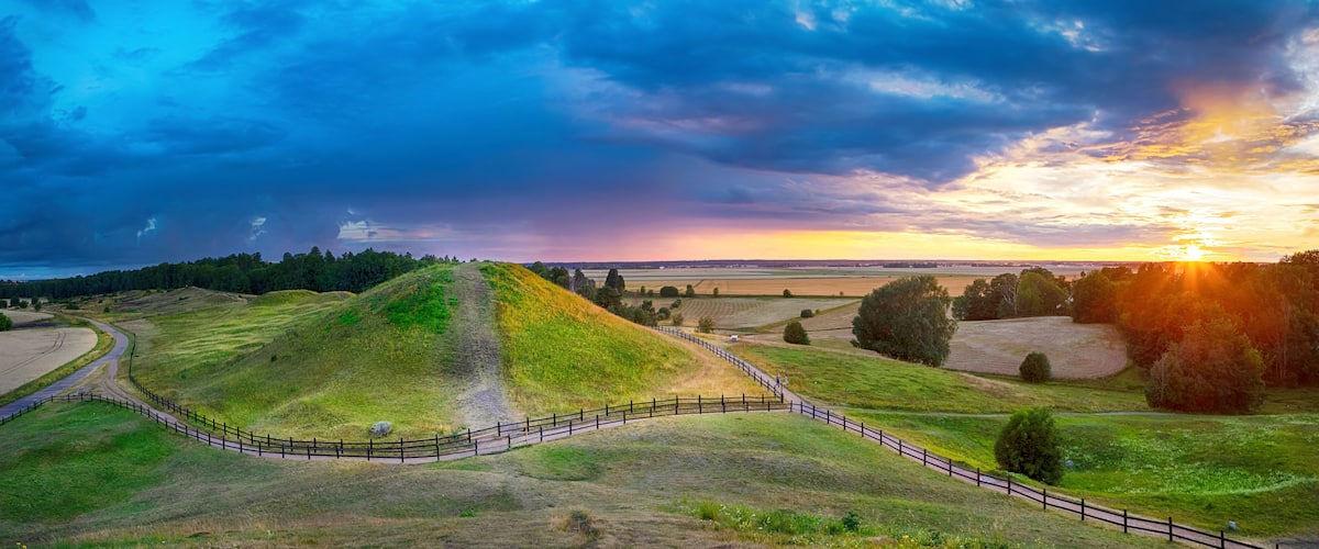 A grassy hill with a fence, a winding path, and a sunset in the background.