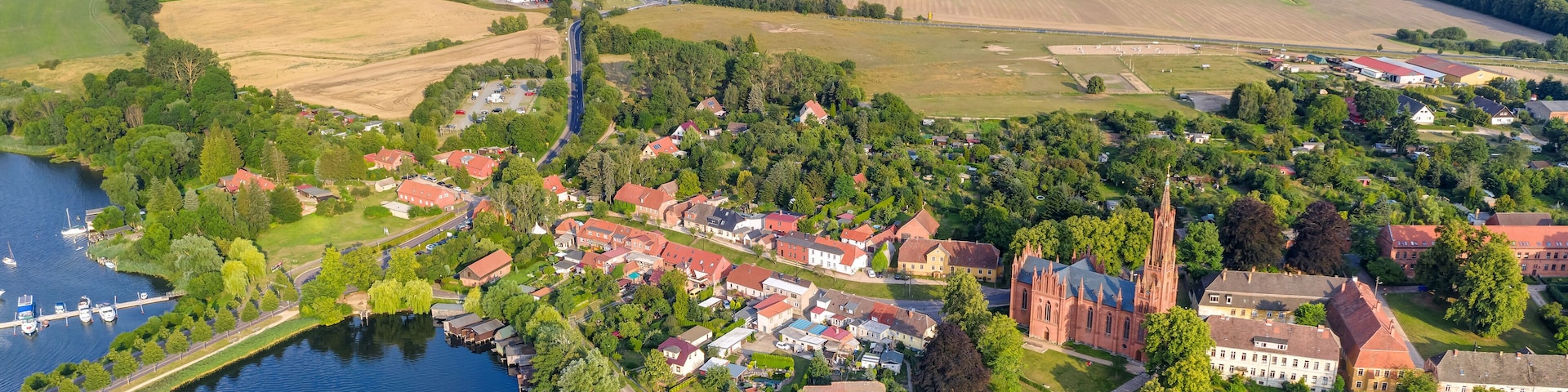 Vista aérea de un pueblo a orillas de un río, con una iglesia destacada, zonas residenciales y campos de cultivo.