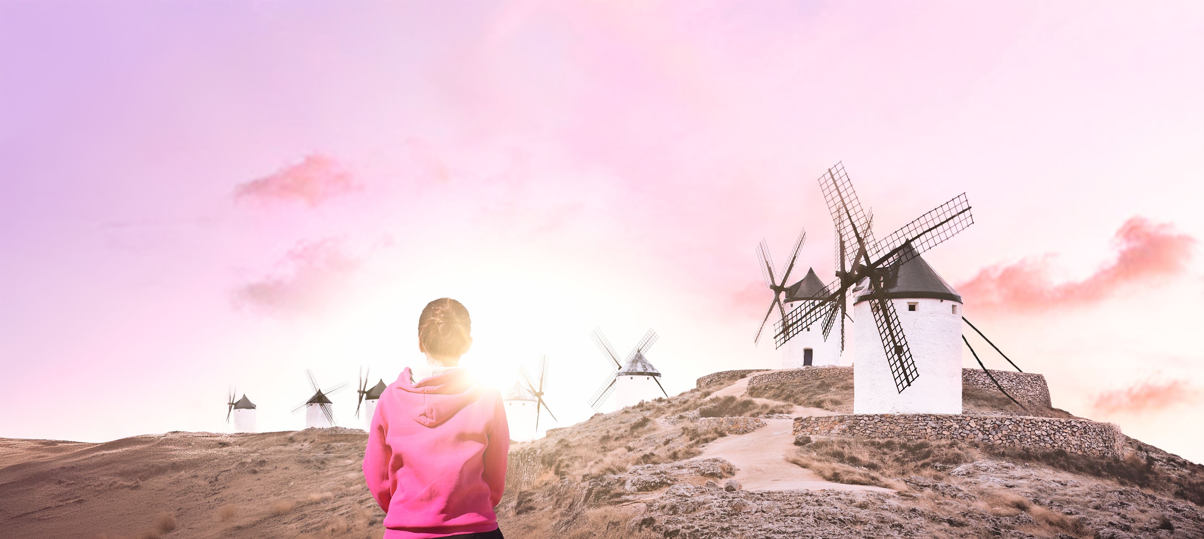 A person in a pink hoodie standing on a hill with windmills in the background.