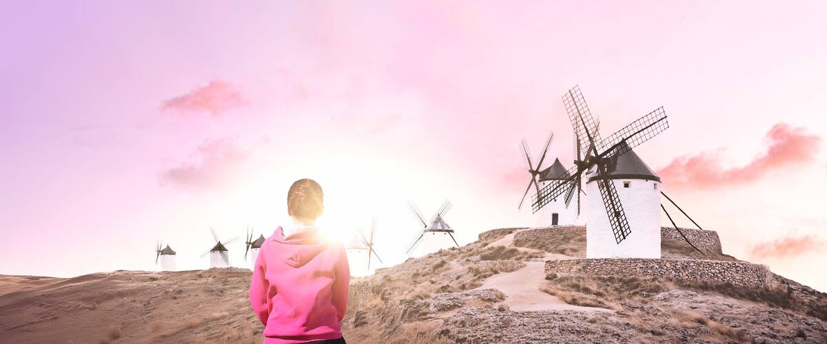 A person in a pink hoodie standing on a hill with windmills in the background.