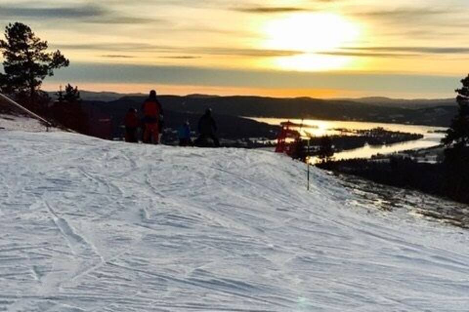 A snowy landscape with a sunset, a ski slope, and a body of water in the distance.
