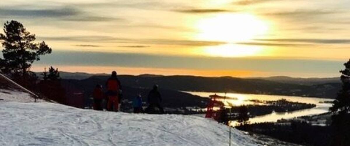 A snowy landscape with a sunset, a ski slope, and a body of water in the distance.