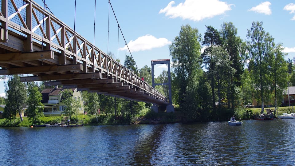 A wooden bridge over a river with houses and trees on the banks.