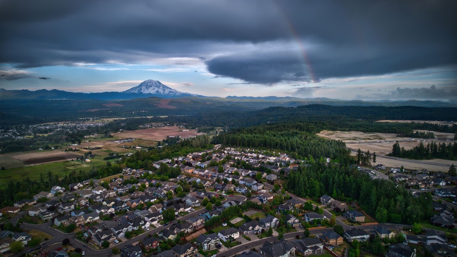 Photo taken from a drone of a faint rainbow of vibrant colors dimly illuminating a thin section of cloudy skies surrounding Mt. Rainier, Washington.