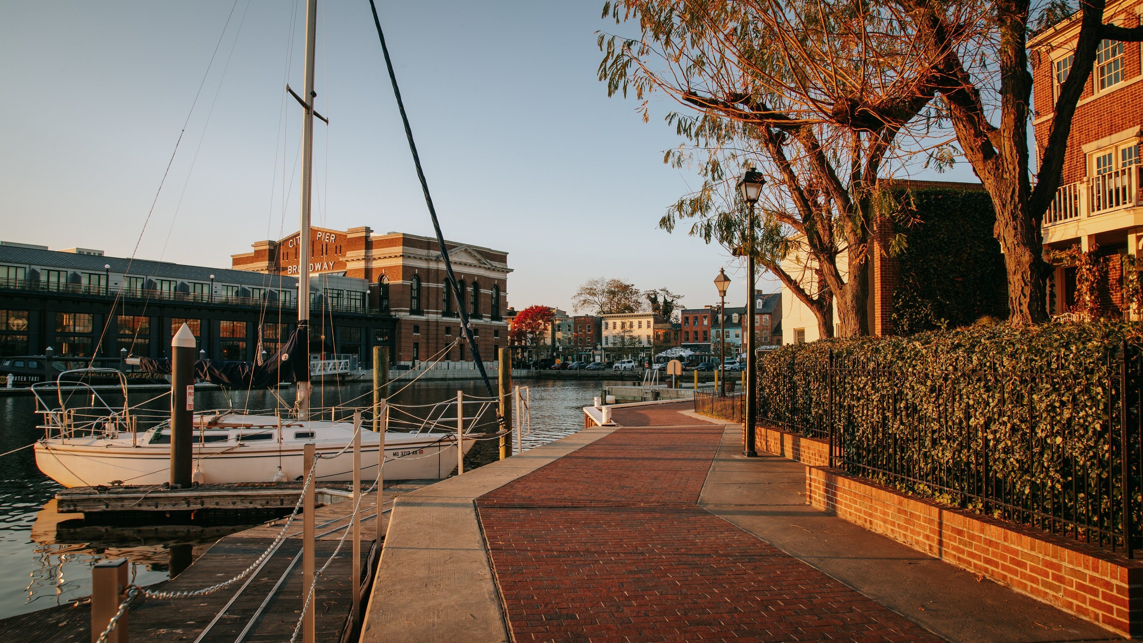 A waterfront with a dock, a sailboat, and buildings along the riverbank.