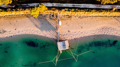 An aerial view of a beach with clear turquoise waters, a wooden pier, and a small structure.