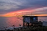 Une jetée en bois s’étendant sur une étendue d’eau au coucher du soleil, avec un ciel aux couleurs vives.