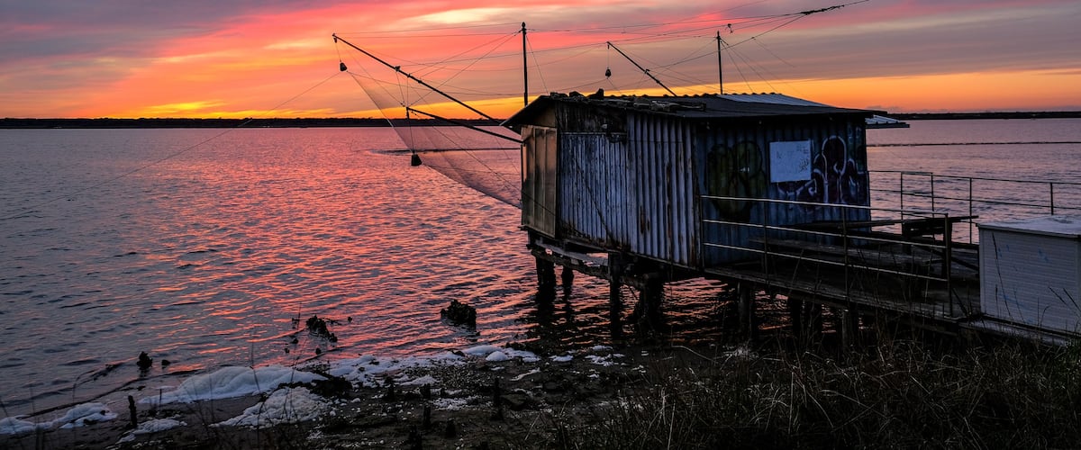 A wooden pier extending into a body of water during sunset with a colorful sky.