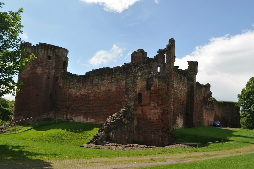 A large, historic brick castle with a grassy foreground and a clear blue sky.