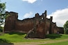 A large, historic brick castle with a grassy foreground and a clear blue sky.