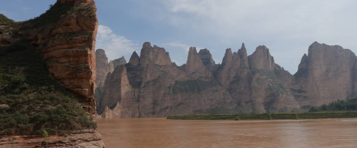 A river with rocky cliffs and a prominent rock formation on the left.
