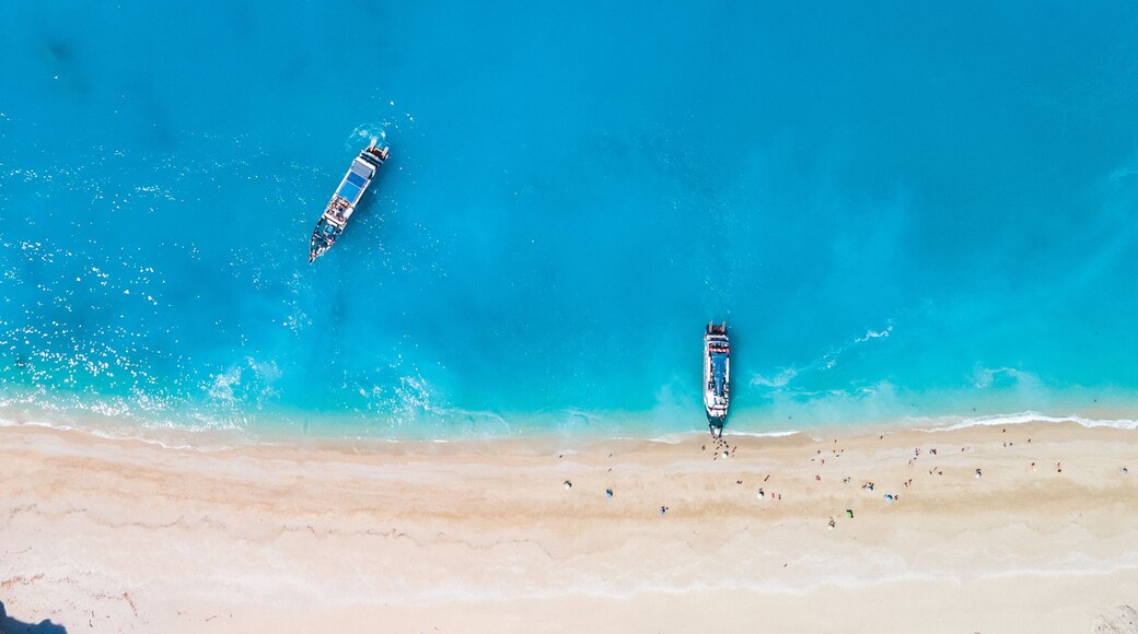 Ein Strand mit klarem tĂŒrkisblauem Wasser, zwei Booten und einem Felsen.