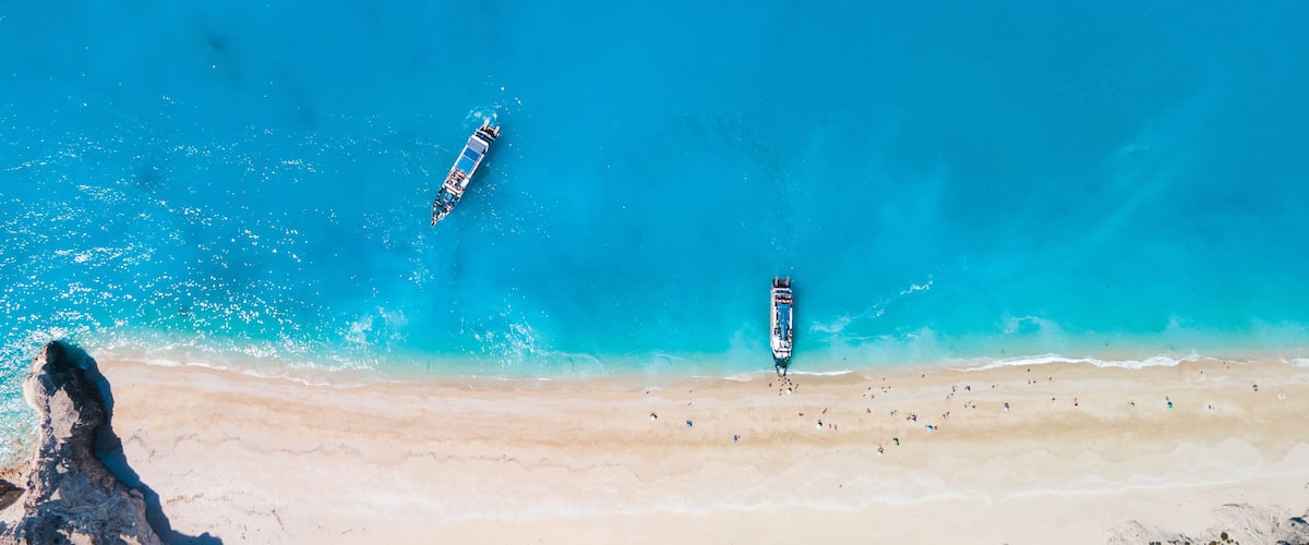 Ein Strand mit klarem türkisblauem Wasser, zwei Booten und einem Felsen.