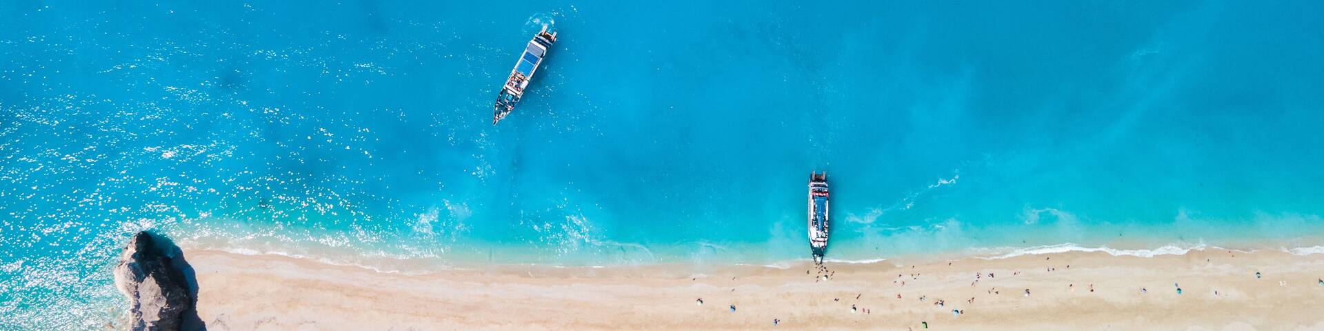 A beach with clear turquoise waters, two boats, and a rocky outcrop.