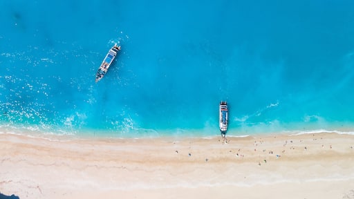 A beach with clear turquoise waters, two boats, and a rocky outcrop.
