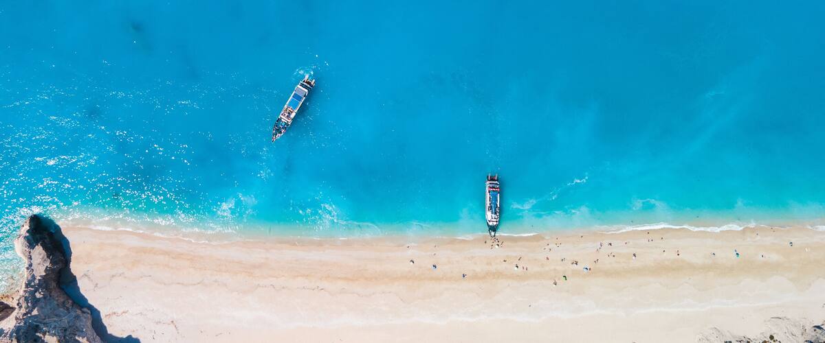 A beach with clear turquoise waters, two boats, and a rocky outcrop.