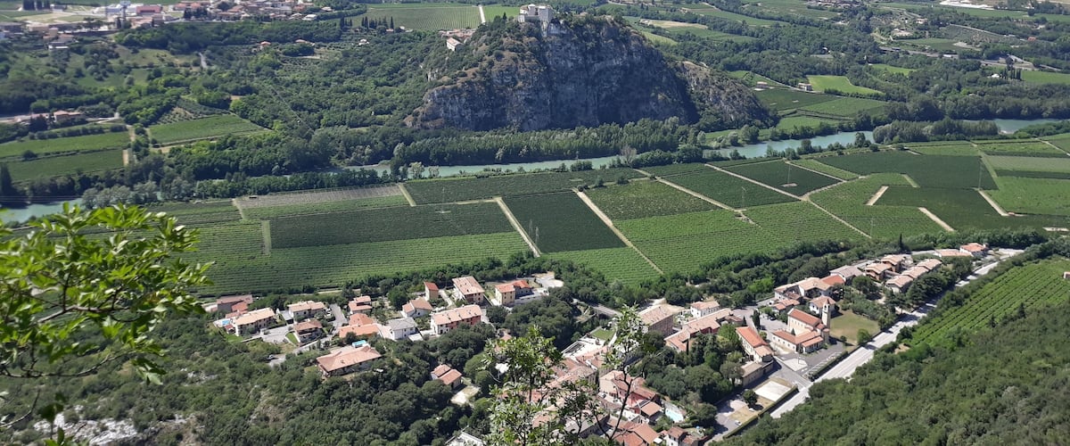A mountainous landscape with a prominent rocky peak, terraced vineyards, and a small village with red-roofed buildings.