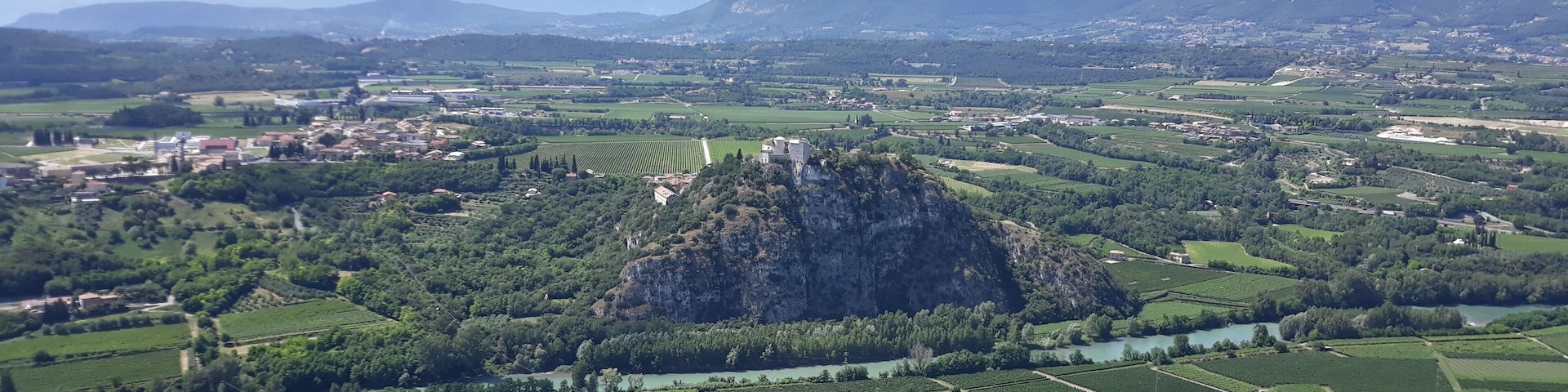 A mountainous landscape with a prominent rocky peak, terraced vineyards, and a small village with red-roofed buildings.