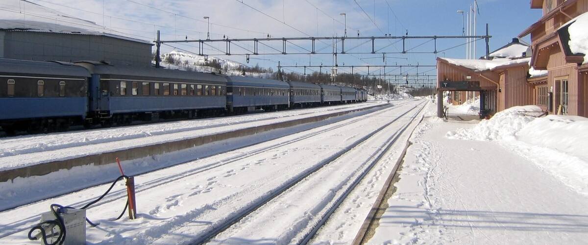 A snow-covered train station with multiple tracks and a train on the left.